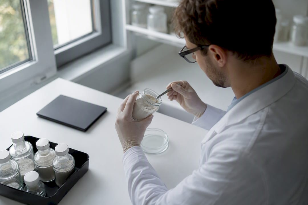 Hænder håndterer prøveflaske med kosttilskudspulver i laboratoriet